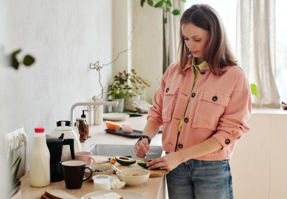 A woman slices an avocado in a bright, modern kitchen with natural light.