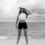 A woman in athletic attire poses near the ocean with a dramatic sky in Natal, Brazil.